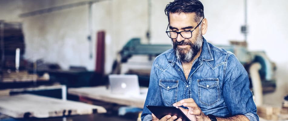 Mann sitzt in seiner Werkstatt und analysiert auf seinem Tablet verschiedene Pensionskassenlösungen
